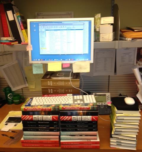 A photograph of stacked books raising the level of a computer to create an impromptu standing desk. 